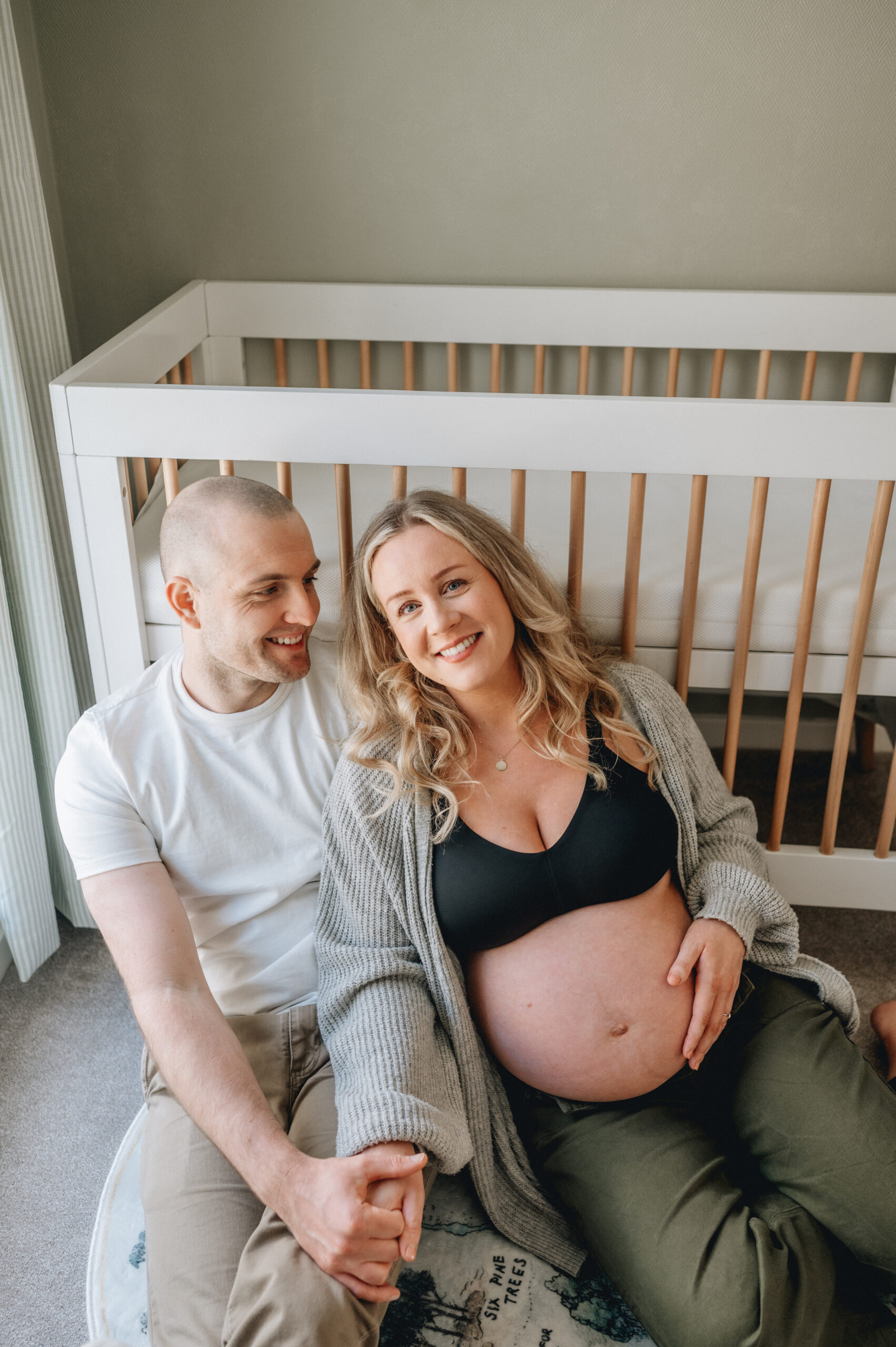 Expectant Mum with her bump and husband next to a crib